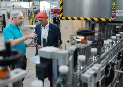 Zwei Männer betrachten eine frische PET-Flasche in einer Produktionsstätte von EPROPLAST, umgeben von Maschinen und Flaschen auf einem Fließband.