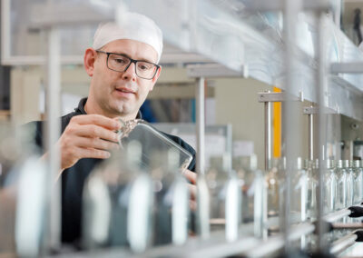 Ein Mitarbeiter von EPROPLAST in Arbeitskleidung kontrolliert eine klare Flasche auf einer Produktionslinie in einer Fabrik.